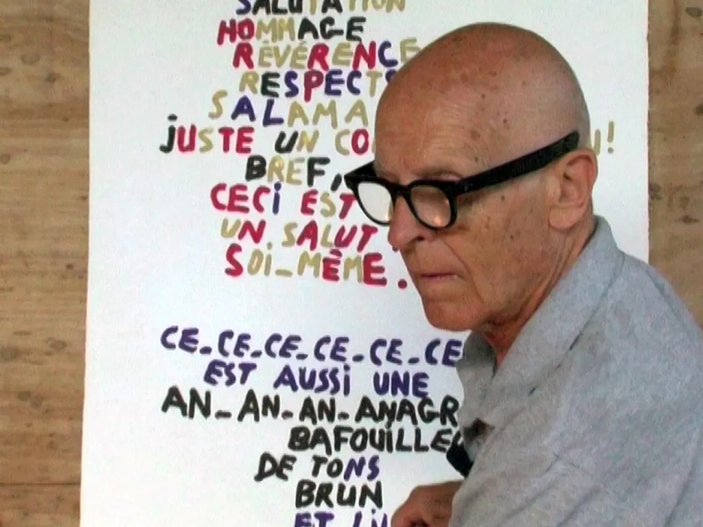 Vidéogramme du film d'Alexandre Gérard "To Look at the Invisible" filmant une visite de l'atelier de Jean Dupuy en compagnie de l'artiste. Le visage de Jean Dupuy devant une de ses œuvres, un anagramme.