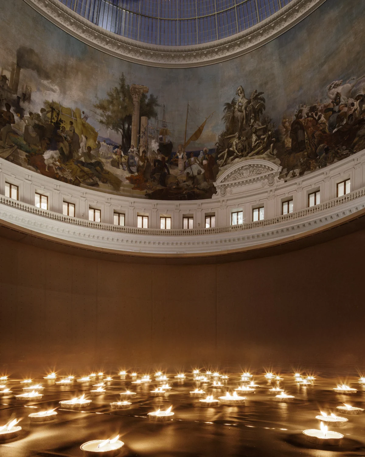 Installation de Renaud Augus-Dormeuil dans la Rotonde de la Bourse de commerce collection Pinault. I Will Keep A Light Burning. Sous la coupole vitrée de la Rotonde de la Bourse de Commerce transformée en observatoire céleste, il donne ainsi corps aux lignes du ciel de demain. Allumées au fil de la soirée, des bougies font peu à peu apparaître une constellation du futur, en un immense cercle matérialisant l’invisible, la carte du ciel de Paris dans 100 ans.